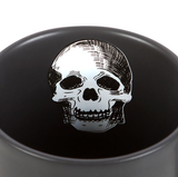 A black mug with a white skull pattern inside and the words Just Trying To Feel Alive in gold written on the outside with white skull, moon and stars showing everyone how your day is going while you enjoy a nice warm drink.