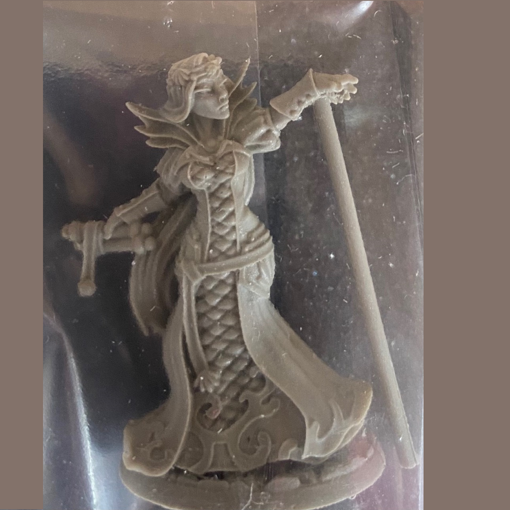 Reaper miniatures. This elegant sorceress is dressed in a long gown with dramatic collar, holding a scroll in one hand and the other outstretched in front of her.