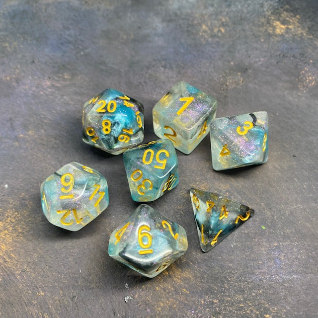 A set of 7 glitter dice having bold gold numbers and suffused with blue colours and glitter.