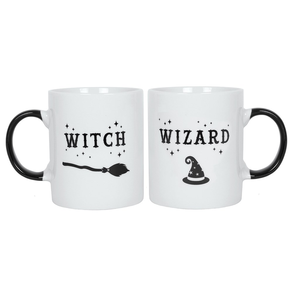 two white mugs with white inside and black handles, one mug has a picture of a broomstick and the word Witch the other has a picture of a hat and says wizard.