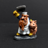 Hand painted dwarf butcher from the Reaper Miniatures range. Mrs MLG has painted this dwarf butcher with a yellow, blue and white colour scheme with a vibrant beard holding a clever above his head and a cute pig under his arm. 