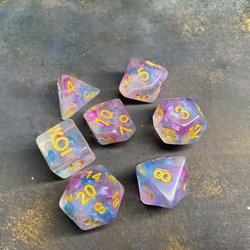 A set of glitter translucent dice suffused with purple, blue and pink colours and glitter. The numbers on these dice are gold and bold. 