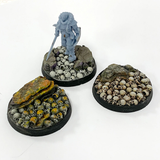 A pack of five resin 40mm bases adorned with skulls and rocks by Legend Games shown with miniature 