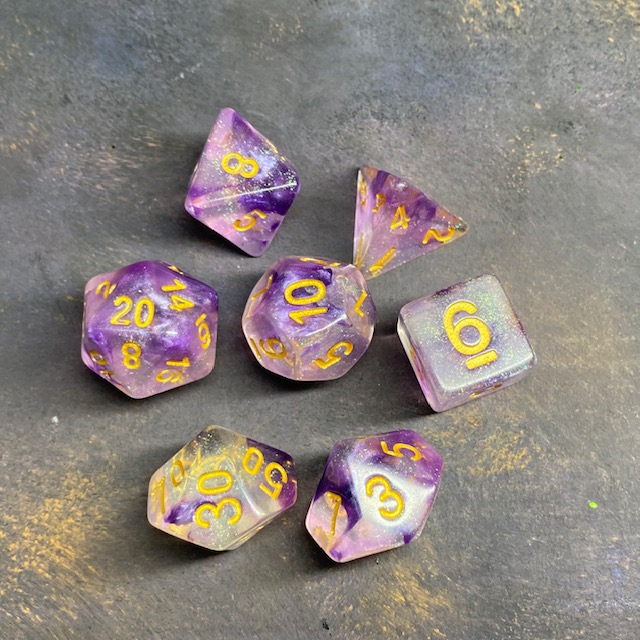 A set of glitter translucent dice suffused with purple colours and glitter. The numbers on these dice are gold and bold.