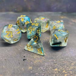 A set of 7 glitter dice having bold gold numbers and suffused with blue colours and glitter.
