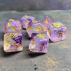 A set of glitter translucent dice suffused with purple colours and glitter. The numbers on these dice are gold and bold. 