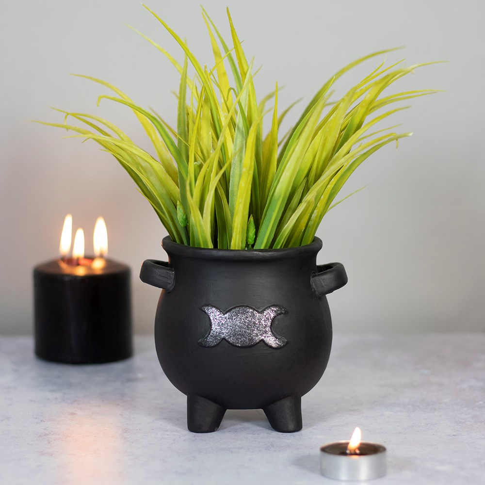 black terracotta cauldron shaped pot adorned with a silver triple moon design shown with green plant and candles