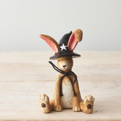 Sitting Witch Rabbit. A fun and charming resin bunny with a black bow and wearing a black witches hat featuring a white star on the front with the rabbits ears poking out of the top