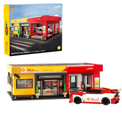 A toy building-block set showing a Shell service station building with a red and yellow station structure and a red-and-white Shell-branded car, displayed in front of its retail box on a white background. CaDA Shell Service Station C66025W brick model