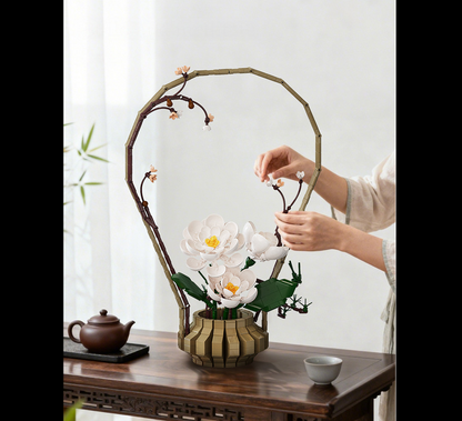 CaDA Winter Silence Oriental Floral Art. Person arranging flowers in a decorative vase on a wooden table with a teapot and cups.