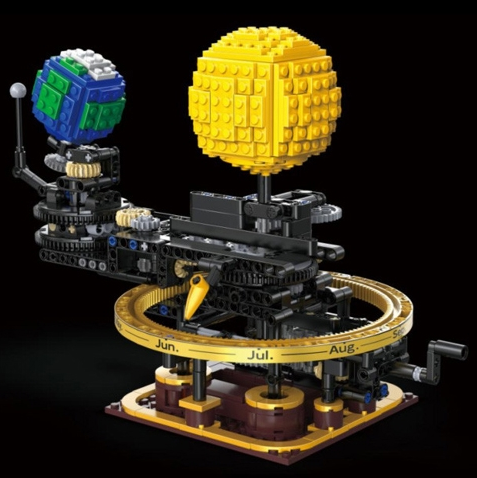 A building-block model of a mechanical calendar or sundial display on a black background. The structure includes a large yellow globe-like sphere, a blue and green globe-like sphere, a circular gold ring with month labels, and black and gold mechanical-looking supports. CaDA Mini Mechanical Solar System 651-piece STEAM building brick kit