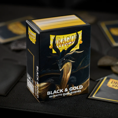 Box of Dragon Shield black and gold sleeves with a dragon illustration on a dark surface. Dragon Shield Black & Gold Matte Dual Sleeves