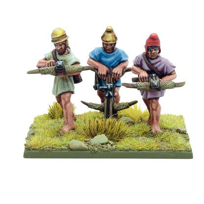 Warlord Games Hail Caesar Gastrophetes 28mm metal artillery crew miniatures. Three miniature figures of people working on a wooden object with grass and rocks below.