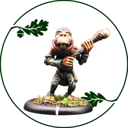A painted fantasy miniature figurine of a small ape-like creature holding a staff, standing on a mossy base with an oak leaf and acorn motif in the background on a white field. Hillfolk Chornicrow by Oakbound Studio
