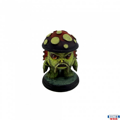 A small green monster figurine with a mushroom cap on its head, standing on a round base against a plain white background.