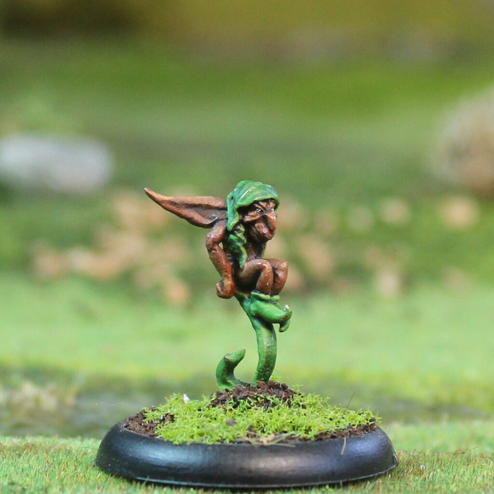 Oakbound Studio Sprite. Miniature figurine of a fairy on a green base with a blurred natural background