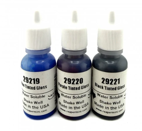 Three small water-soluble tinted gloss bottles with white caps on a white background. The bottles are labeled 29219 Blue Tinted Gloss, 29220 Purple Tinted Gloss, and 29221 Black Tinted Gloss, with Reapermini branding visible on the labels. Reaper MSP Tinted Glosses Triad #2