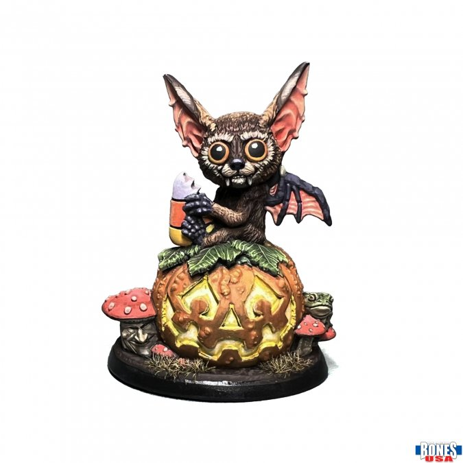 Reaper Miniatures 30178 Halloween Batling. whimsical scene features an adorable bat creature perched atop a carved jack-o’-lantern, clutching a piece of candy corn. Around the base of the pumpkin sit sculpted details including a small frog and clustered mushrooms