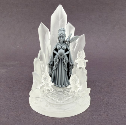 A detailed fantasy figurine of a crowned fairy or goddess standing among tall translucent crystal spires on a circular base, photographed against a plain gray studio background. Liora Emervale Dawnfire