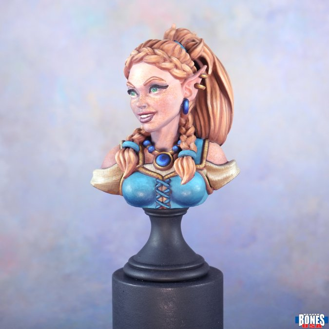 A painted fantasy elf bust sculpture on a black display base, featuring long braided light brown hair, blue eyes, a blue and gold outfit, and blue earrings, photographed against a soft pastel blue background. Ryelle Rainheather Bust