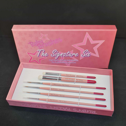 Ruby Brushes Signature Six paint brush set with Kolinsky sable and drybrushes in presentation box.. Pink brush set in a box with 'The Signature Six' branding on a black background