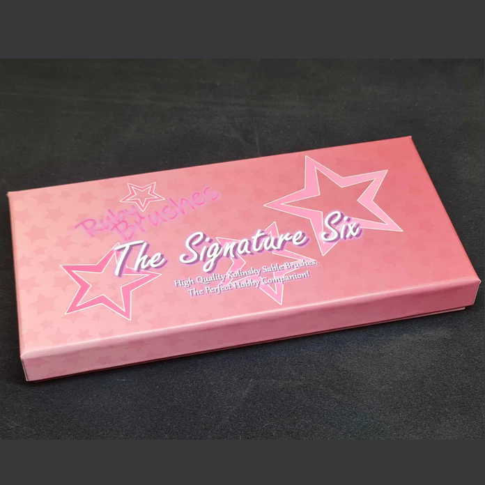 Ruby’s Paint Studio Signature Six miniature painting brush set for tabletop hobbyists. Pink box with 'The Signature Six' branding on a black background