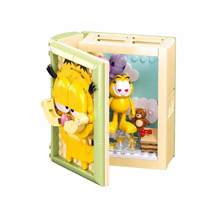 A toy building-block set featuring a beige cabinet or safe with an open door, containing a yellow Garfield figure and a small teddy bear, with another yellow Garfield figure outside the cabinet. Sluban Garfield Book 230 piece LEGO-compatible brick building kit with bedroom diorama