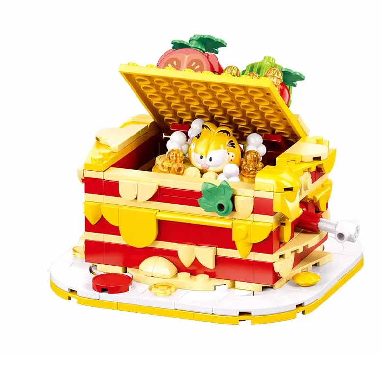 A colourful toy building-block set featuring a red and yellow treasure chest with an open lid, gold coins, fruit pieces, and a small cat figure inside, photographed on a clean white background. Sluban Garfield Lasagna 250 piece brick building kit with hidden Garfield figure and storage box