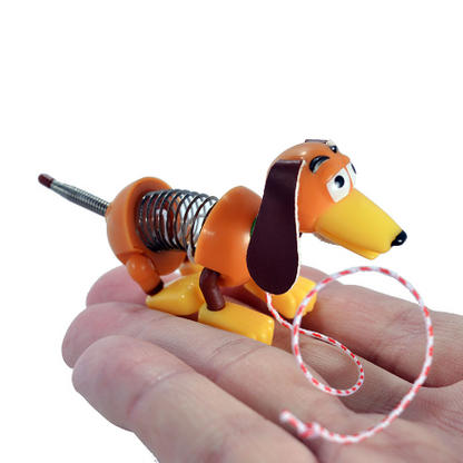 A small orange and yellow spring-dog toy held in a person's hand against a plain white background. World's Smallest Collector's Edition Slinky Dog miniature pull toy