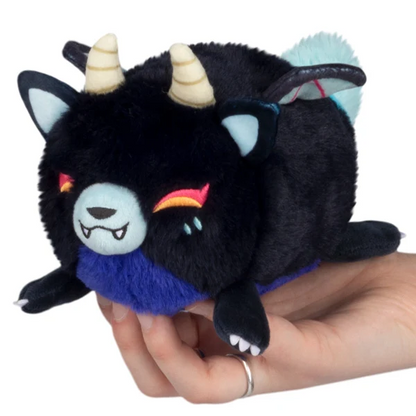 A small black plush creature toy with cream horns, a blue belly, and colourful embroidered facial details, being held in a person's hand against a plain white background. Squishable Demon Kitsune - Alter Egos Baby Kitsune Series 15