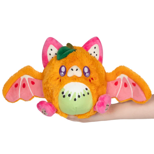 Plush toy resembling a fruit with bat wings held by a hand on a white background. Squishable Fruit Bat