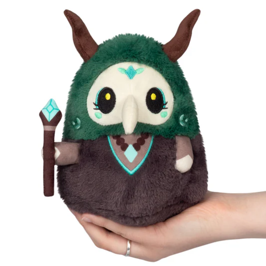 Plush toy with green hood and brown body held in a hand on a white background. Squishable Plague Doctor Forest Queen