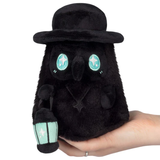 Black plush toy with green eyes and accents held in a hand against a white background. Squishable Plague Doctor Void