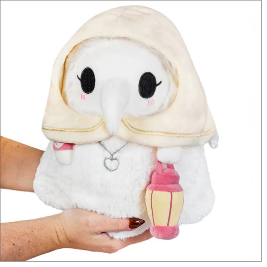 Plush toy resembling a character with a hood, white face, and pink accents held by a person. Plague Nurse
