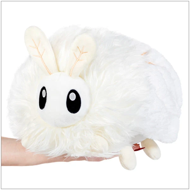 A fluffy white plush toy with large black eyes and leaf-patterned cream ears, being held on a person's hand against a plain white background. Squishable Poodle Moth