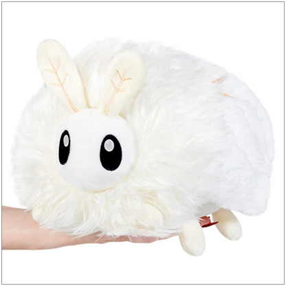 A fluffy white plush toy with large black eyes and leaf-patterned cream ears, being held on a person's hand against a plain white background. Squishable Poodle Moth