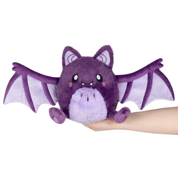 Purple plush bat toy held in a hand against a white background. Squishable Spooky Bat plush toy with magnetic wings purple and lilac colouring
