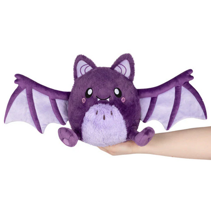 Purple plush bat toy held in a hand against a white background. Squishable Spooky Bat plush toy with magnetic wings purple and lilac colouring