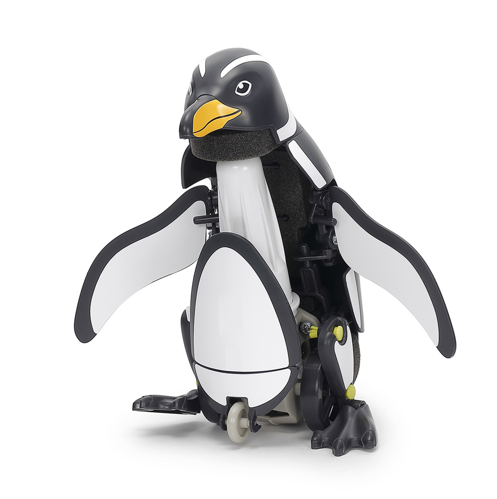 A penguin-shaped mobility chair or wheelchair with black and white body panels, a yellow beak, and visible mechanical wheels and support structure, photographed on a clean white studio background. Tamiya Walking and Swimming Penguin mechanical assembly kit