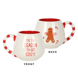 rounded white mug featuring a red and white stripe handle, the words 'Tis The Season To Get Cosy' on one side and a gingerbread on the other.