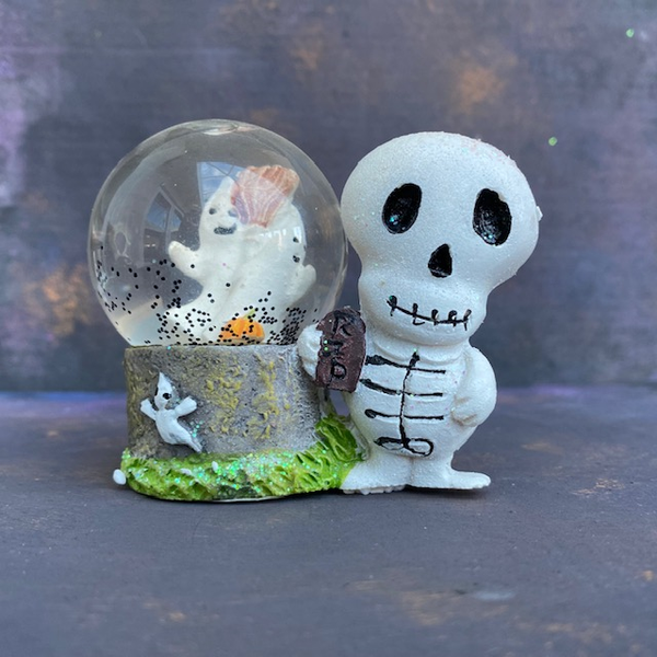 Spooky waterball - his ornament features a skeleton holding an RIP plaque under one arm, he is next to a globe which has black 'snow' and two ghosts either side of a broom. 