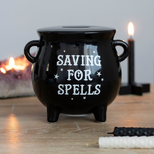 A black cauldron design money box with white 'saving for spells' text on the front