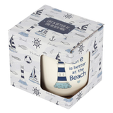 a boxed A pretty nautical themed mug with a white and blue pallet of colours, a lighthouse image and the words 'Life is better at the beach', the box has nautical images on it  