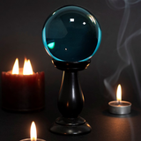 A beautiful teal crystal ball and stand in a dark background with candles