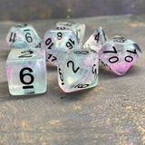 A set of 7 glitter dice having black numbers and suffused with glitter and pink swirl. 