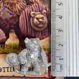 he Battle Bear by Northumbrian Tin Solider is a metal miniature of a teddy bear holding a sword in one hand and a shield in the other, with a button for one eye and a patch on his chest. shown here with a ruler 
